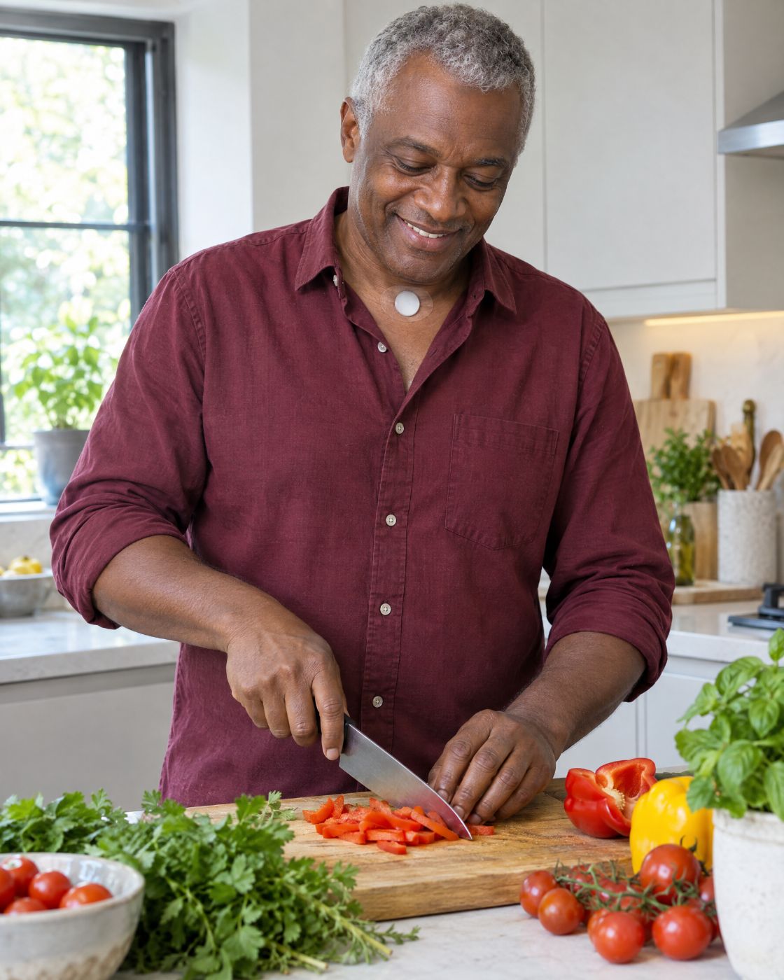 A man in a burgundy shirt chops vegetables in his kitchen, an HME visible at the base of his neck.